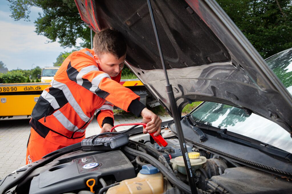 Vejhjælper starter bilen med en jumpstarter under motorhjelmen på en Volkswagen.