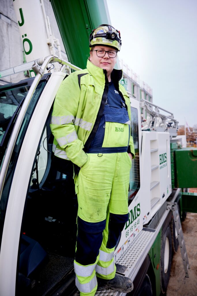 Kranfører fra BMS i sikkerhedshjelm står på kranens trinbræt ved førerkabinen.