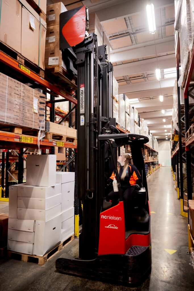 Truckfører kører reach-truck og henter varer på øverste lagerhylde.